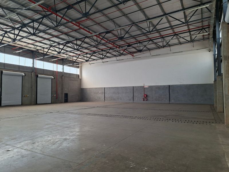 Spacious industrial warehouse unit featuring high ceilings with exposed steel trusses, concrete flooring, and multiple roller shutter doors for efficient access.