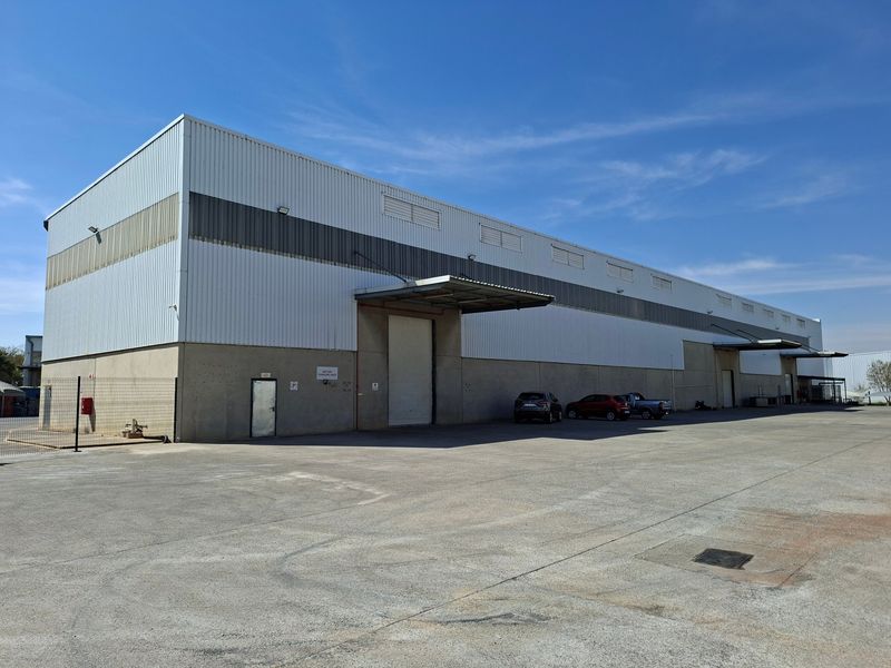 Industrial warehouse facility featuring corrugated metal cladding, multiple roller shutter loading doors with canopies, and a large concrete yard area.