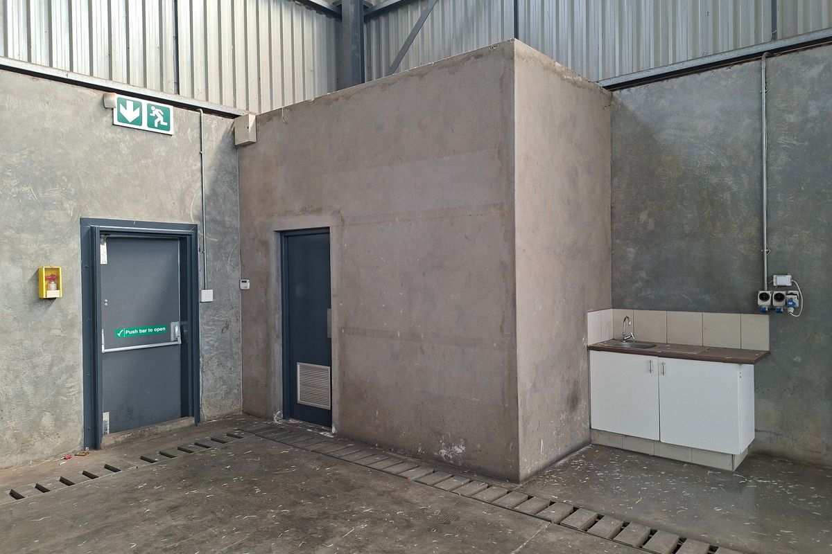 Industrial utility space featuring concrete walls, metal cladding, an emergency exit, and a small kitchenette area with a sink and base cabinetry.