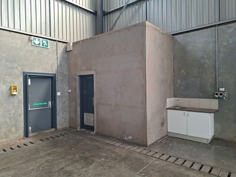 Industrial utility space featuring concrete walls, metal cladding, an emergency exit, and a small kitchenette area with a sink and base cabinetry.
