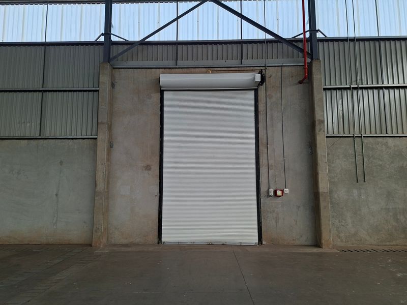 Industrial warehouse interior featuring a large roller shutter door, exposed steel structural elements, and durable concrete wall and floor finishes.