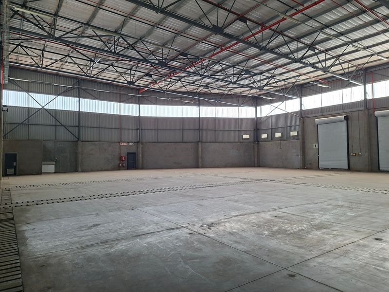 Spacious industrial warehouse featuring high ceilings with exposed steel trusses, concrete flooring, and large roller shutter doors for efficient access.