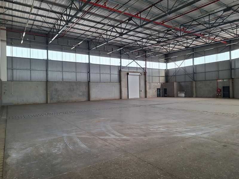 Spacious industrial warehouse featuring high ceilings with exposed steel trusses, fire sprinkler system, concrete flooring, and a large roller shutter door for easy access.