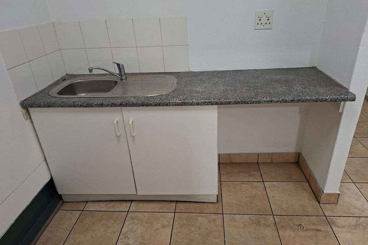 A functional kitchenette area featuring a stainless steel sink, granite countertop, tiled splashback, and ceramic floor tiles, suitable for office or utility use.