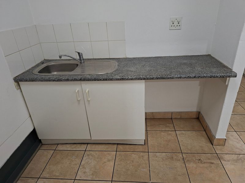 A functional kitchenette area featuring a stainless steel sink, granite countertop, tiled splashback, and ceramic floor tiles, suitable for office or utility use.