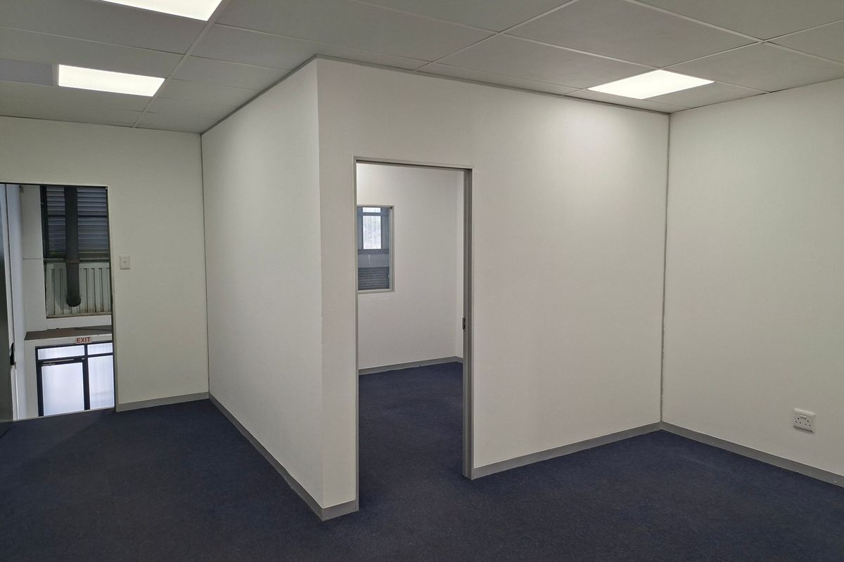 A clean, vacant office space featuring neutral walls, carpeted flooring, and modern recessed ceiling lighting, suitable for a professional workspace.