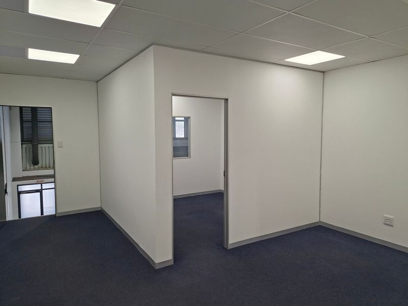 A clean, vacant office space featuring neutral walls, carpeted flooring, and modern recessed ceiling lighting, suitable for a professional workspace.