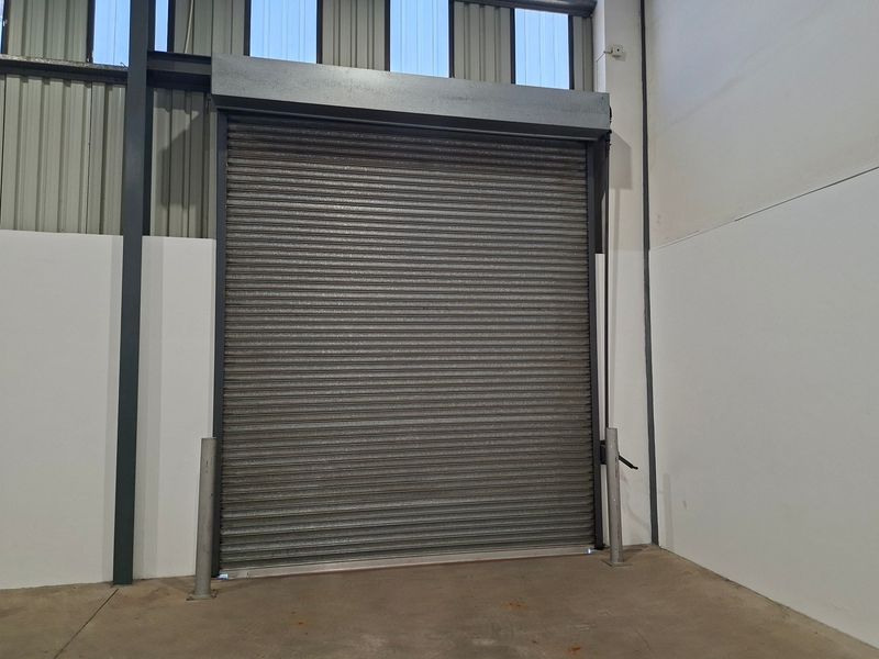 Industrial warehouse space featuring a large metal roller shutter door, exposed steel structural framing, and durable concrete flooring.