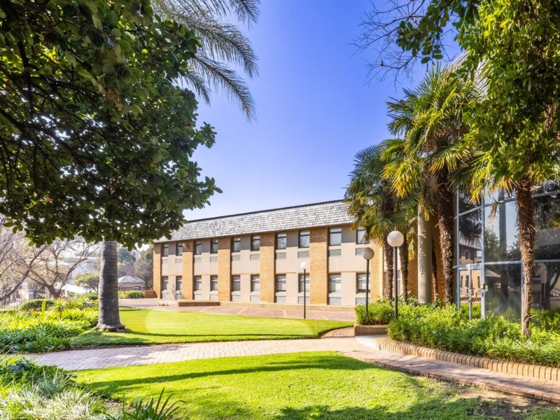 A well-maintained commercial building exterior featuring a brick facade, large glass windows, and landscaped garden areas with paved walkways.