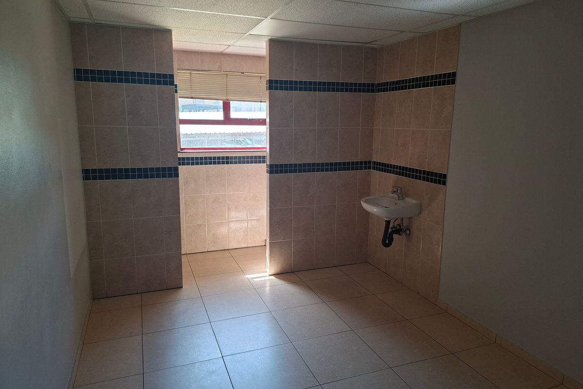 A functional, tiled bathroom space featuring a wall-mounted basin, drop ceiling, and natural light from a window.