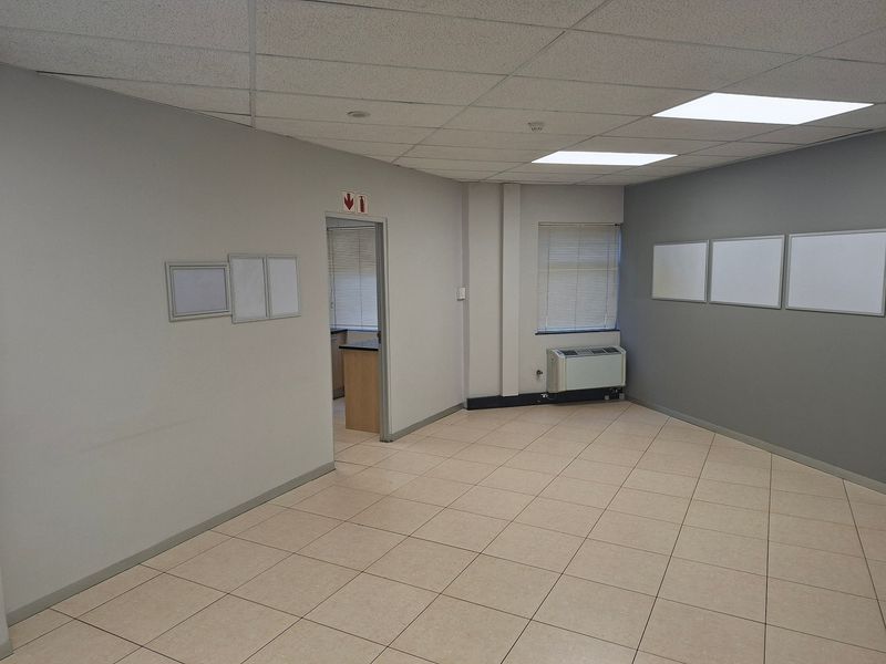 A clean, empty commercial office space featuring tiled flooring, a suspended ceiling with recessed lighting, air conditioning, and wall-mounted whiteboards.