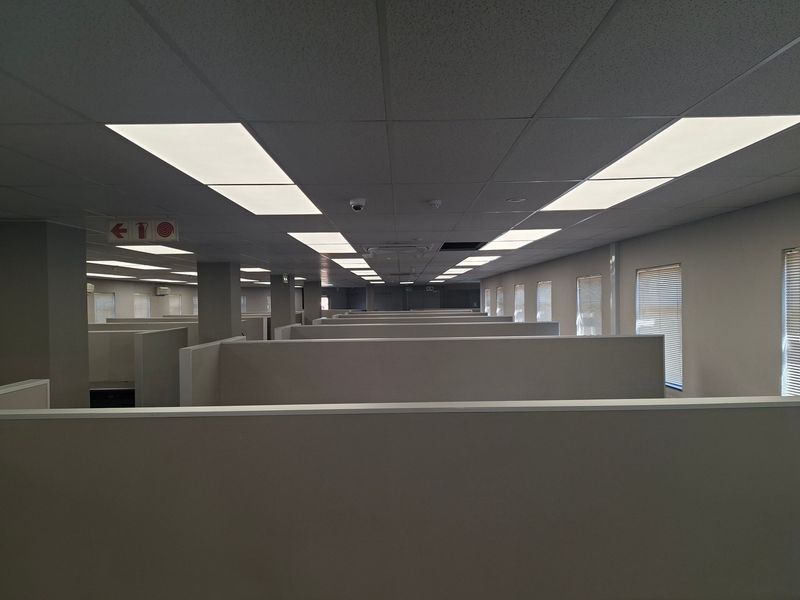 Spacious open-plan commercial office area featuring a suspended ceiling, recessed lighting, and built-in cubicle partitions, providing a functional workspace layout.