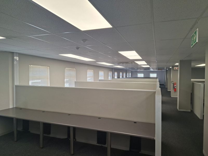Open-plan commercial office space featuring built-in cubicle partitions, integrated desk surfaces, suspended ceilings with recessed lighting, and neutral finishes.