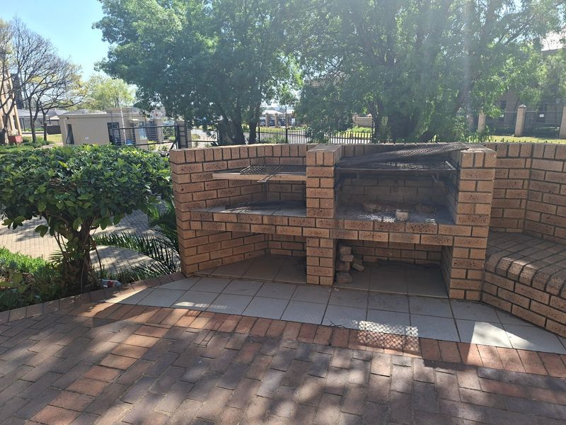 Outdoor patio area featuring a large built-in brick braai and integrated brick seating, set on a paved surface within a landscaped environment.