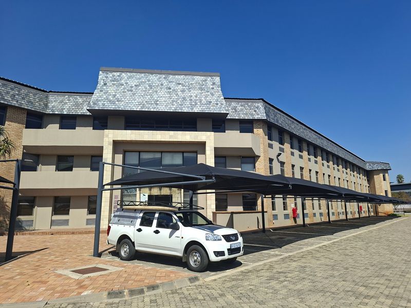 Front elevation of a commercial office building featuring a multi-story brick facade, slate roof, and extensive covered parking bays.