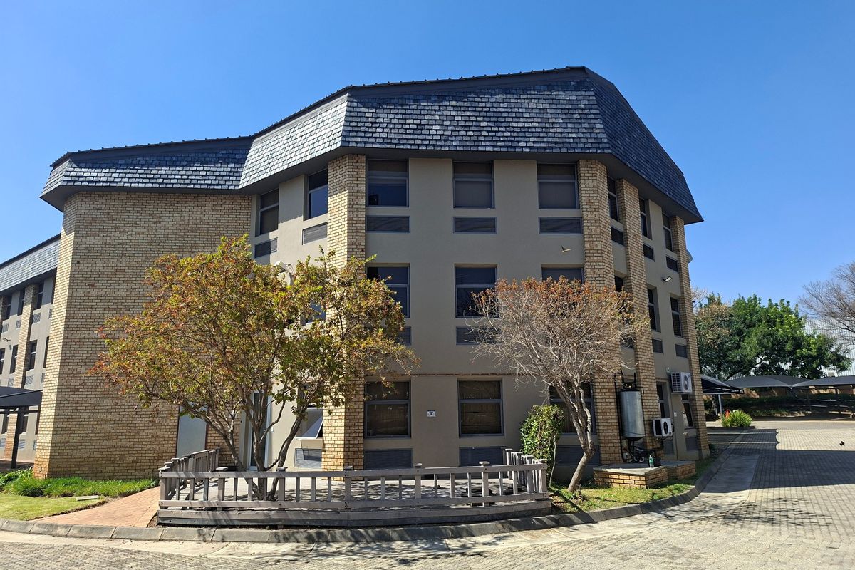 A multi-story commercial building featuring a brick and rendered facade with a slate roof, set within a paved office park environment.