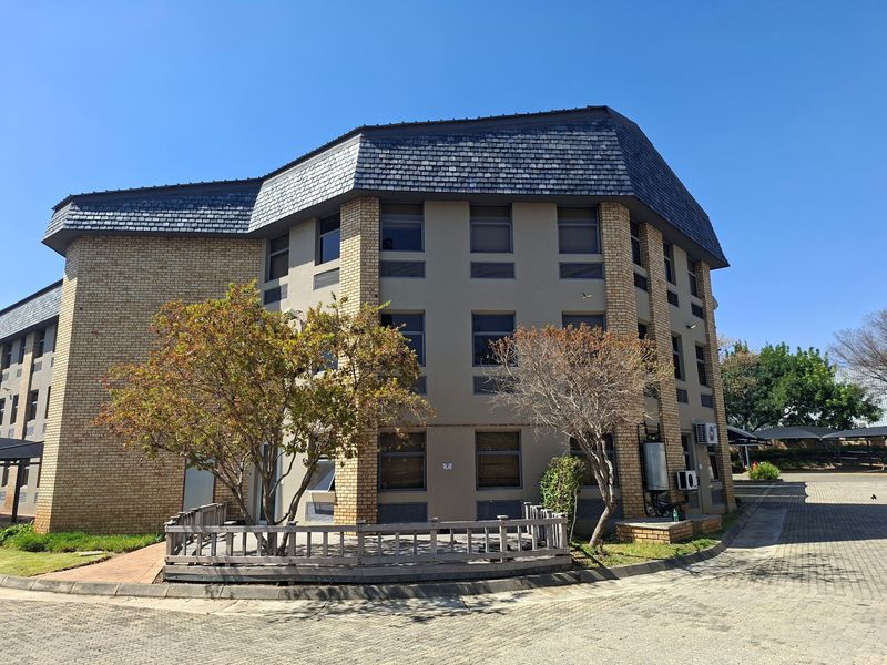 A multi-story commercial building featuring a brick and rendered facade with a slate roof, set within a paved office park environment.