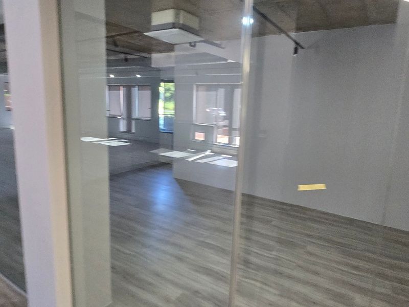 Modern open-plan office space featuring glass partitions, exposed concrete ceilings, and durable laminate flooring, offering a bright and professional work environment.