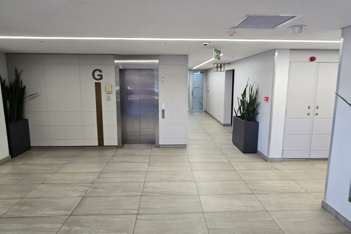 A clean, modern commercial hallway featuring tiled flooring, a stainless steel elevator, and clear directory signage for building occupants.
