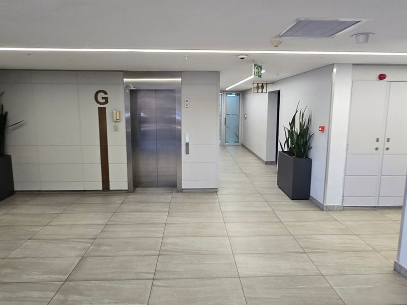 A clean, modern commercial hallway featuring tiled flooring, a stainless steel elevator, and clear directory signage for building occupants.