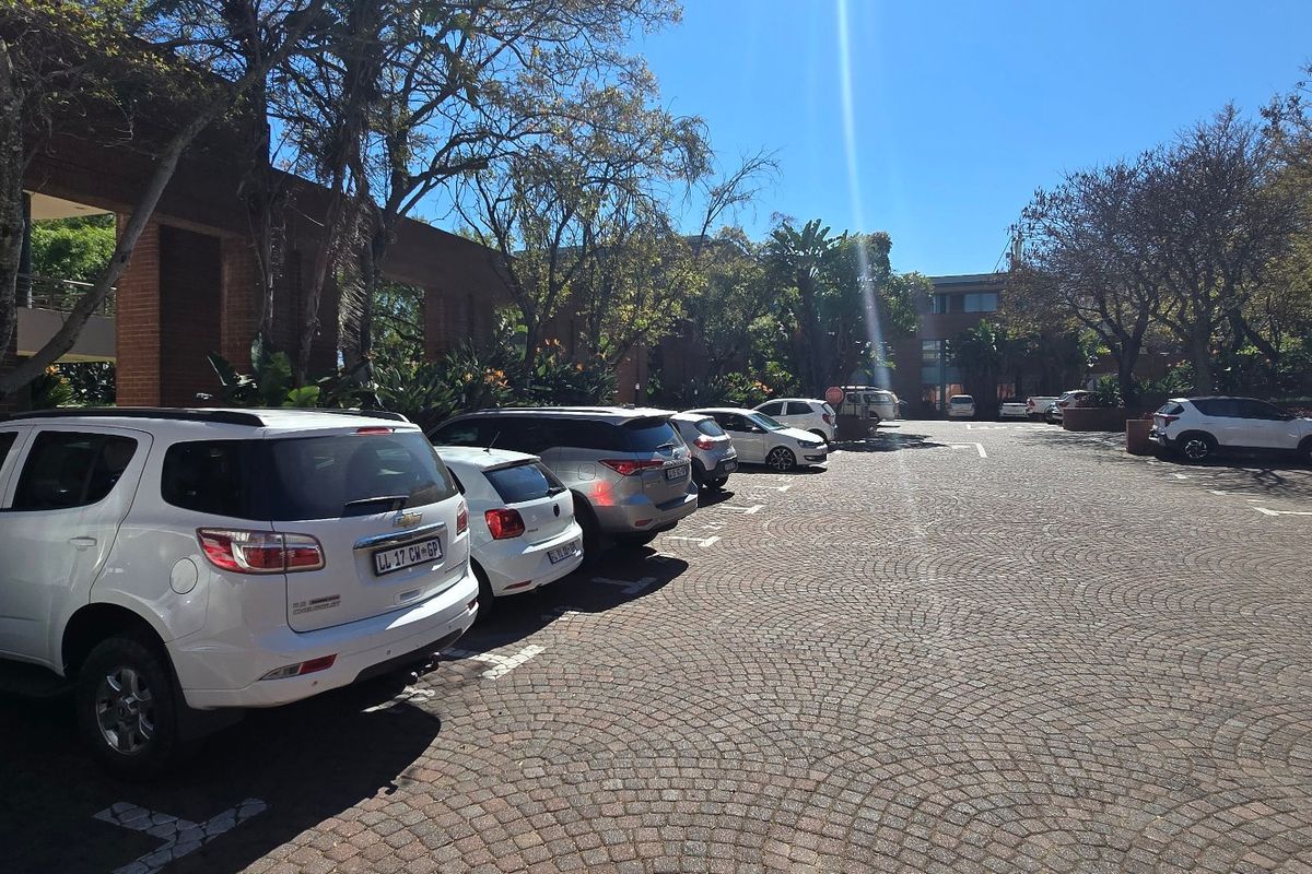 A view of the commercial property's exterior parking area featuring brick paving and established trees surrounding the building facade.