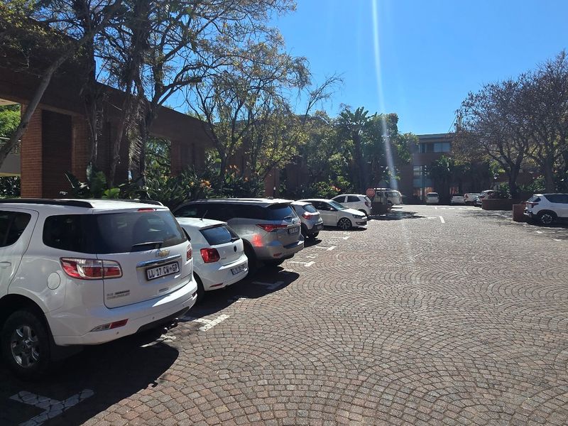 A view of the commercial property's exterior parking area featuring brick paving and established trees surrounding the building facade.