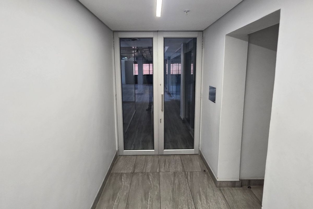A clean, modern hallway featuring tiled flooring, neutral walls, and a double glass door leading into an adjacent office space.
