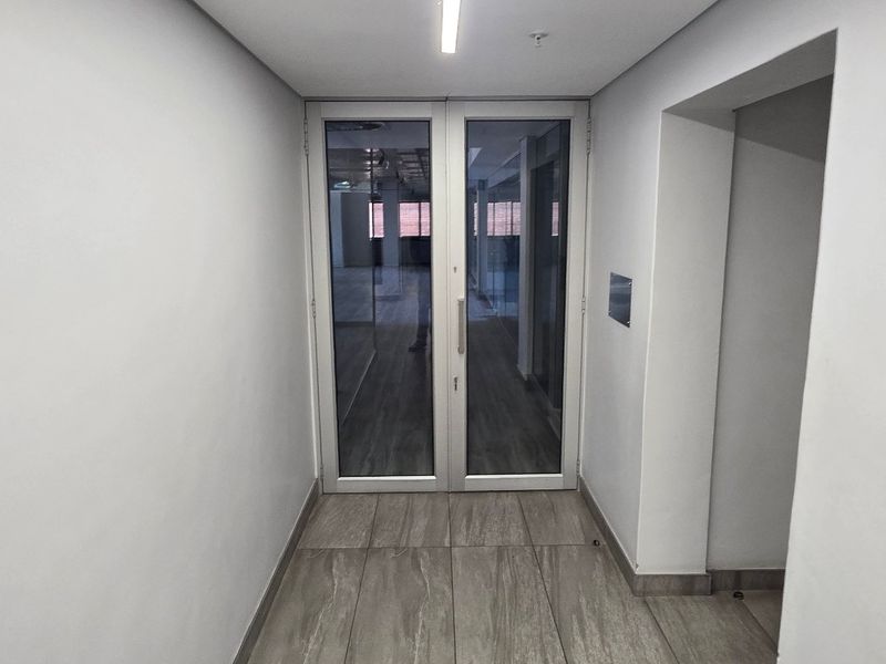 A clean, modern hallway featuring tiled flooring, neutral walls, and a double glass door leading into an adjacent office space.