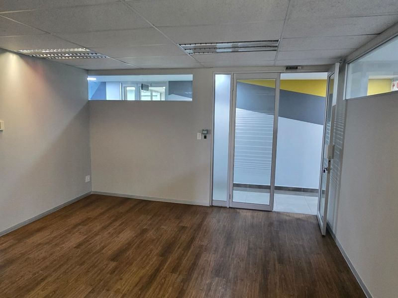 A vacant commercial office space featuring laminate flooring, suspended ceilings with recessed lighting, and glass partition walls.
