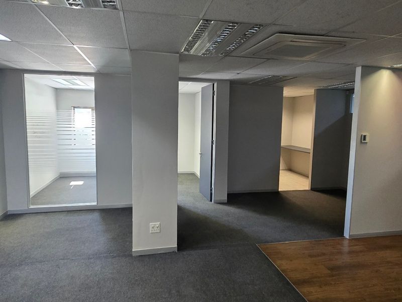 A vacant commercial office space featuring a mix of carpet and laminate flooring, suspended ceilings, and glass-partitioned private office areas.