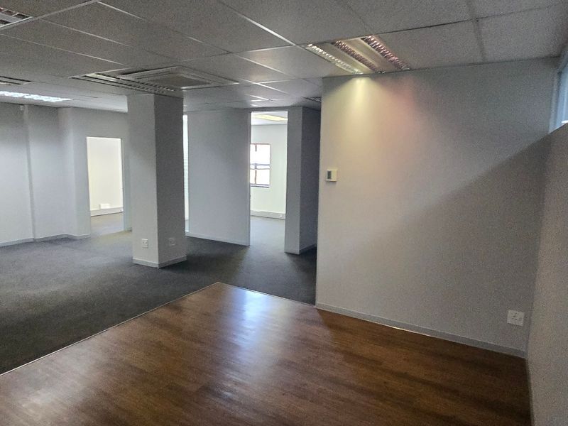 An open-plan commercial office space featuring a mix of carpet and laminate flooring, suspended ceilings, and glass partitioning.