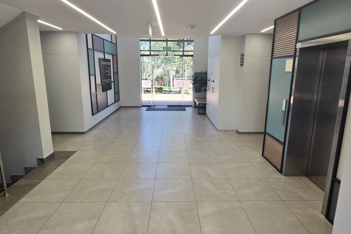 Modern commercial building lobby featuring tiled flooring, recessed linear lighting, elevator access, and a glass entrance door leading to the exterior.
