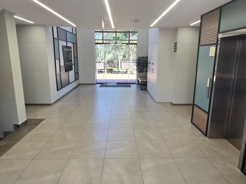 Modern commercial building lobby featuring tiled flooring, recessed linear lighting, elevator access, and a glass entrance door leading to the exterior.