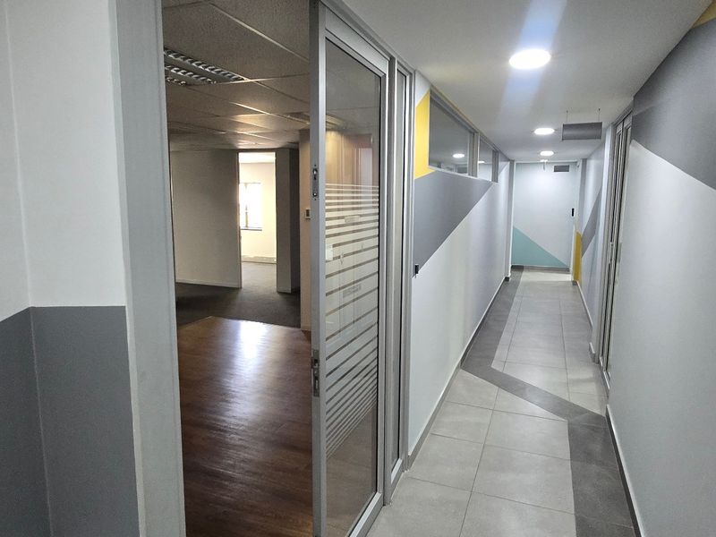 A clean, modern commercial hallway featuring tiled flooring, recessed lighting, and a glass partition door leading into an office space.