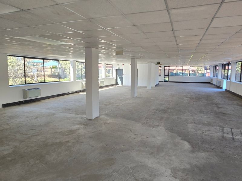 Spacious open-plan commercial office area featuring large windows, suspended ceilings, structural columns, and wall-mounted HVAC units, ready for custom flooring and fit-out.