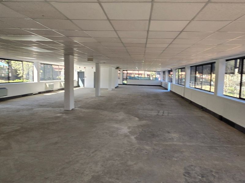 A large, open-plan commercial office space featuring expansive windows, suspended ceilings, and integrated HVAC units, currently in a shell condition.