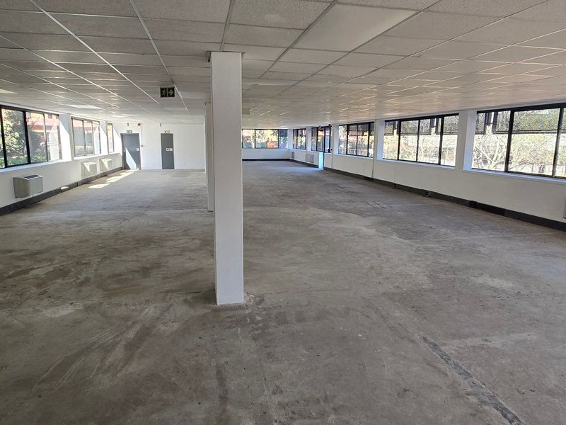 A large, vacant open-plan commercial office space featuring a suspended ceiling, large windows, and wall-mounted HVAC units, ready for custom fit-out.