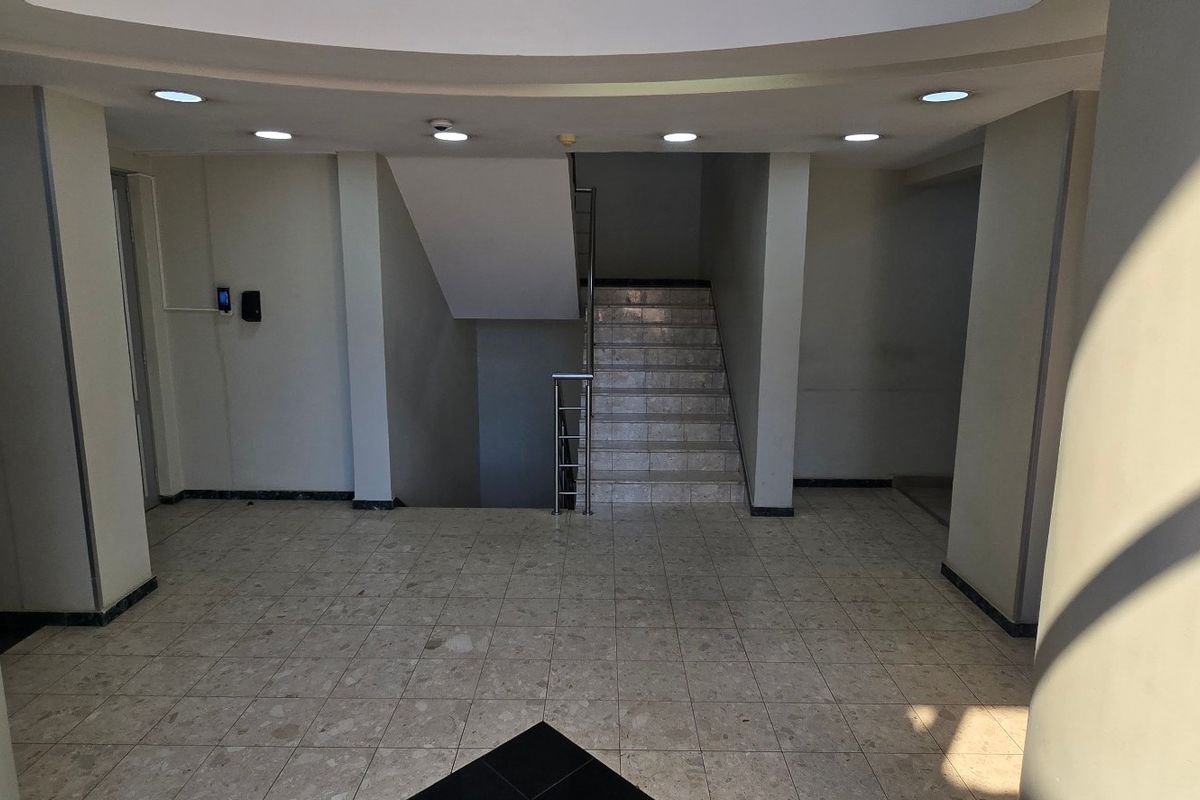 A spacious commercial building entrance lobby featuring tiled flooring, recessed ceiling lighting, and a central staircase with a metal handrail.