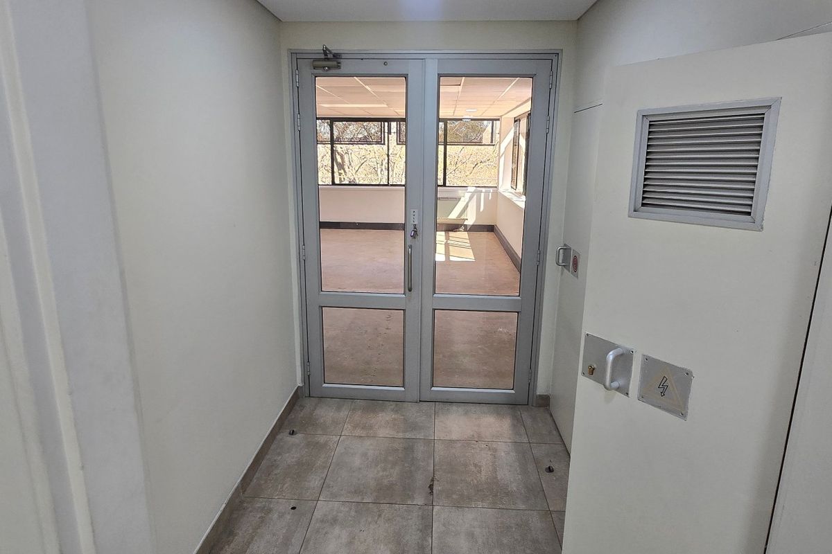 A clean, functional commercial entry area featuring tiled flooring and secure aluminium-framed glass double doors leading into an open-plan office space.