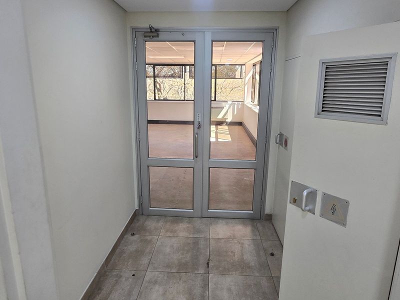 A clean, functional commercial entry area featuring tiled flooring and secure aluminium-framed glass double doors leading into an open-plan office space.