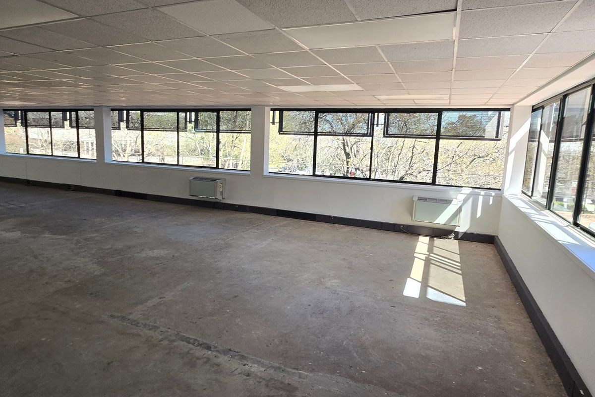 A spacious, vacant commercial office area featuring large windows, suspended ceilings, and wall-mounted air conditioning units, ready for custom fit-out.