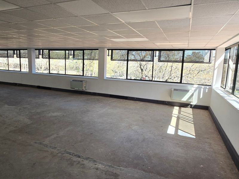 A spacious, vacant commercial office area featuring large windows, suspended ceilings, and wall-mounted air conditioning units, ready for custom fit-out.