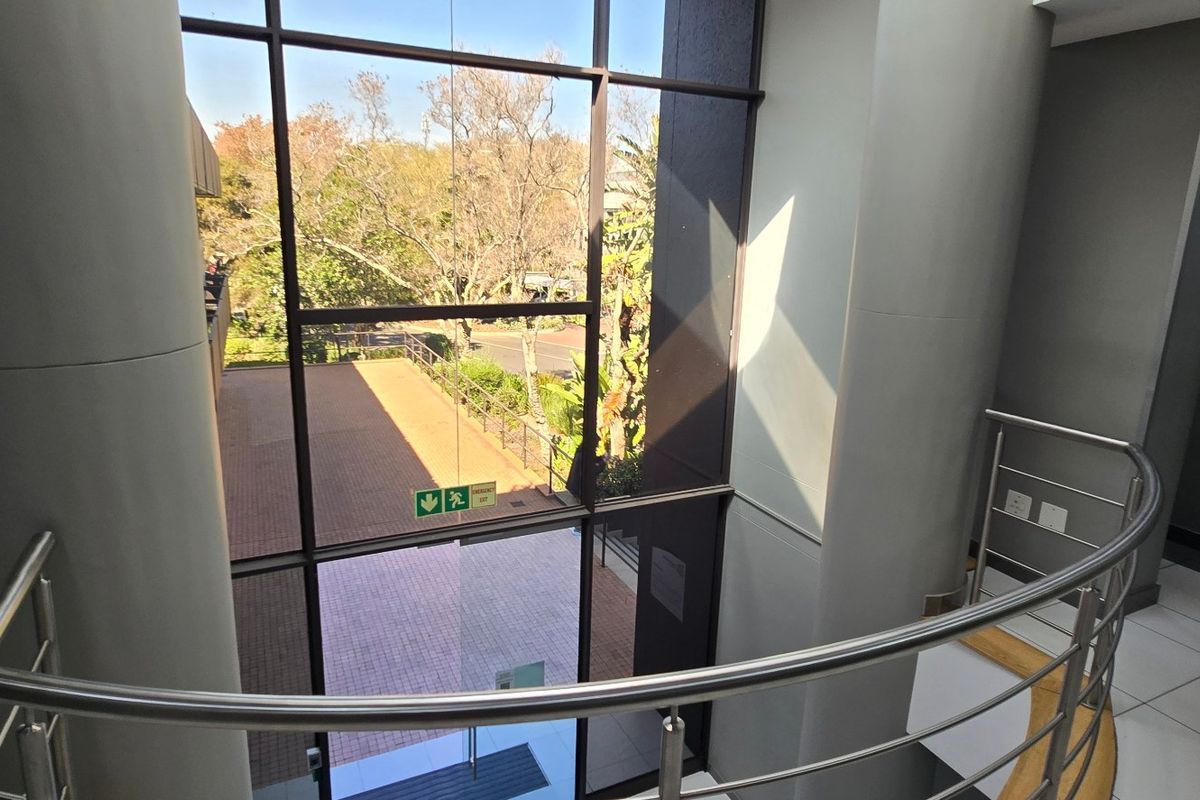 Modern commercial entrance lobby featuring a full-height glass curtain wall, stainless steel balustrade, and clean tiled flooring with views of the exterior grounds.