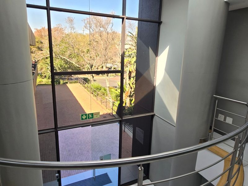 Modern commercial entrance lobby featuring a full-height glass curtain wall, stainless steel balustrade, and clean tiled flooring with views of the exterior grounds.