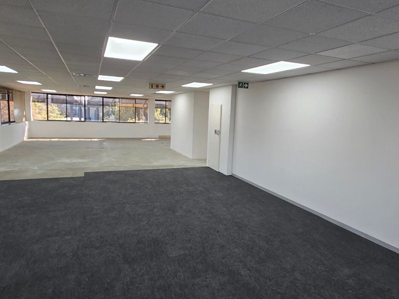 A spacious, open-plan commercial office area featuring large windows, neutral carpeting, and a suspended ceiling with recessed lighting, ready for custom fit-out.
