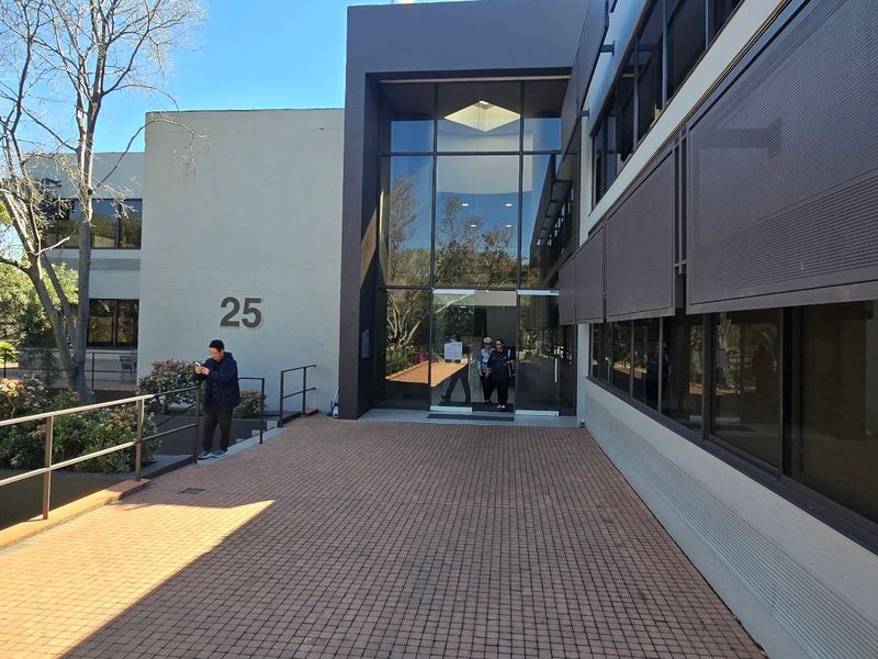 Modern commercial building entrance featuring a glass facade, paved walkway, and external sun louvers, providing a professional and accessible entry point.
