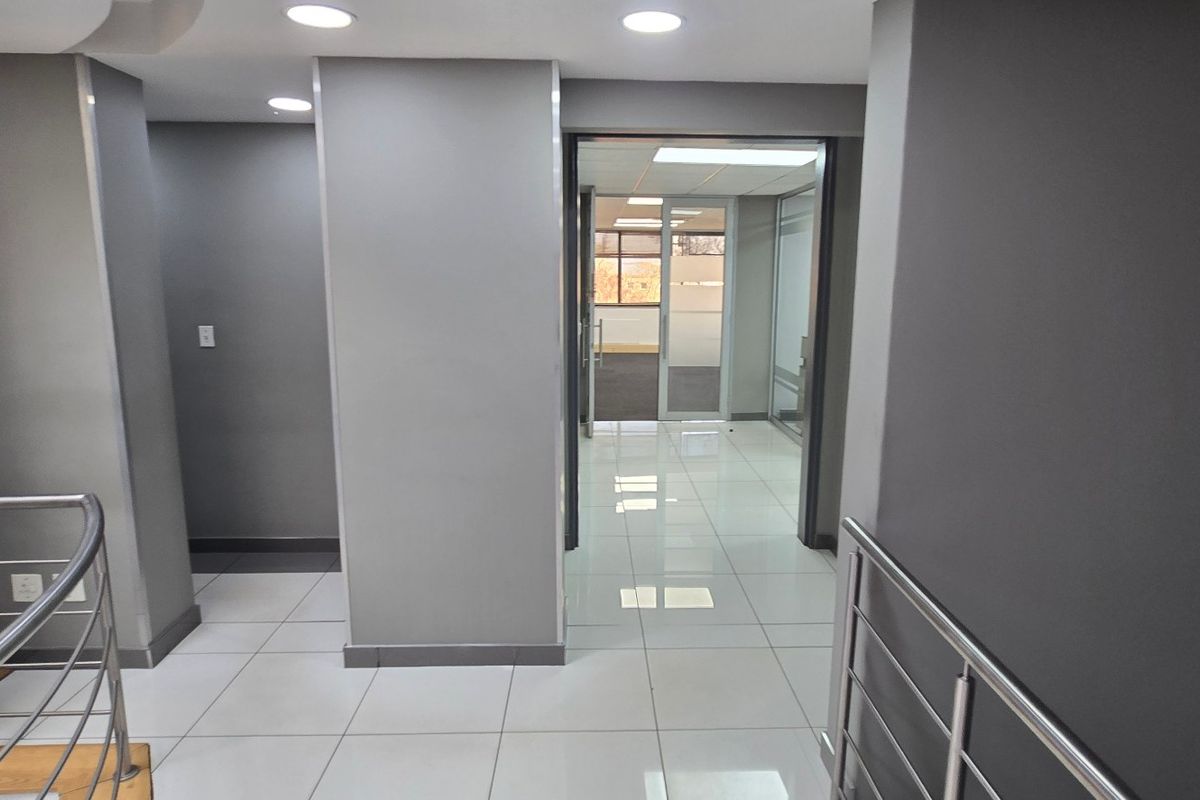 A modern commercial hallway featuring polished porcelain floor tiles, recessed downlighting, and a stainless steel balustrade leading to an office area.