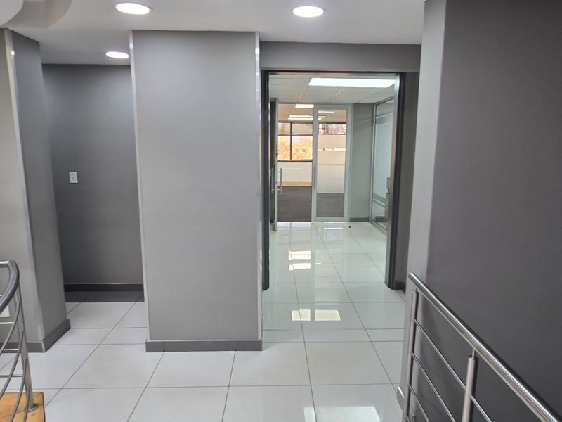 A modern commercial hallway featuring polished porcelain floor tiles, recessed downlighting, and a stainless steel balustrade leading to an office area.