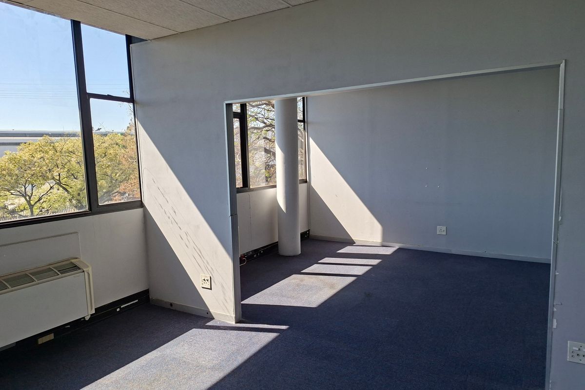 An empty commercial office space featuring large windows, a structural column, and carpeted flooring, offering a blank canvas for professional workspace configuration.