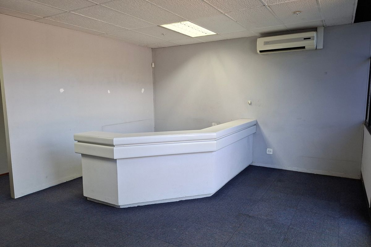 A vacant commercial office space featuring a built-in reception desk, carpeted flooring, suspended ceiling, and a wall-mounted air conditioning unit.